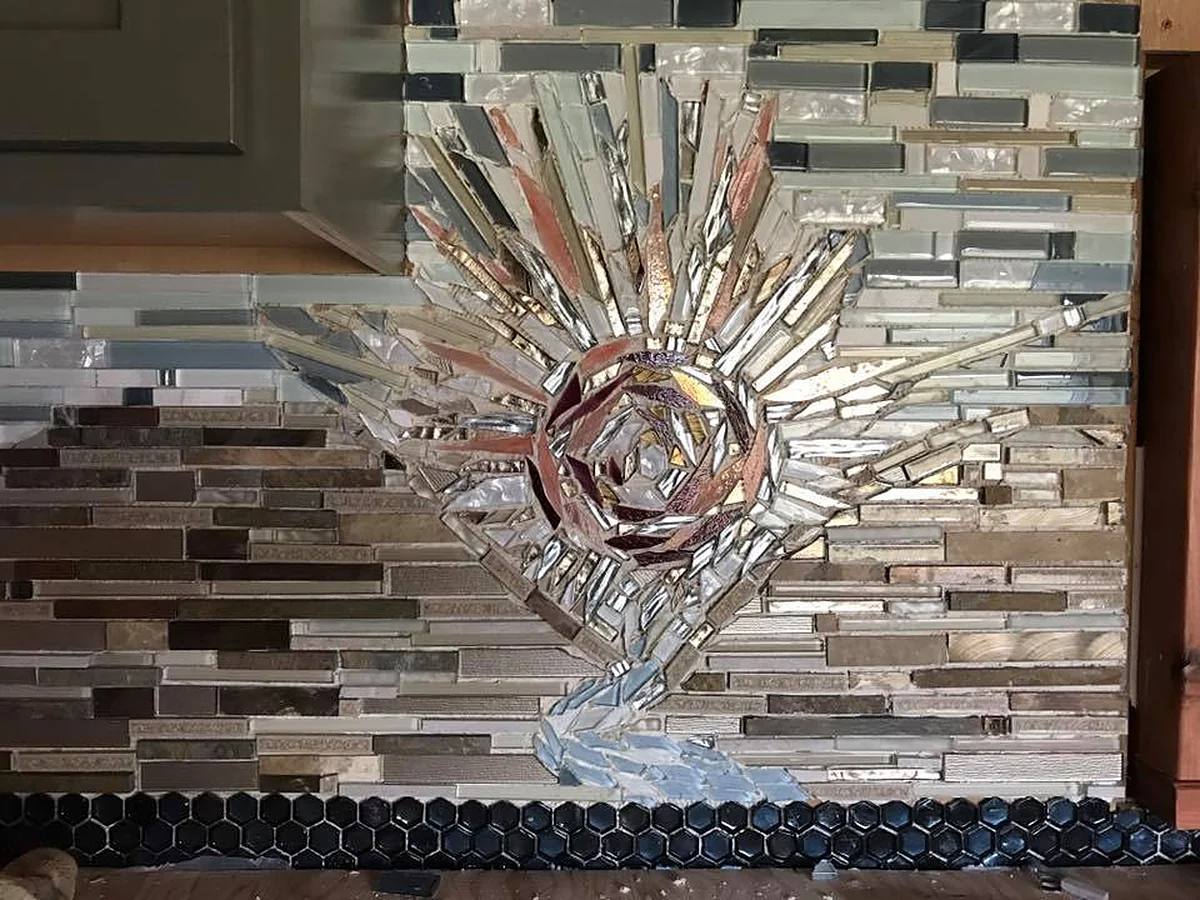 Rose Sunset: a mirror and glass mosaic of a rose-coloured sun bursting out of a striped stone and glass kitchen backsplash